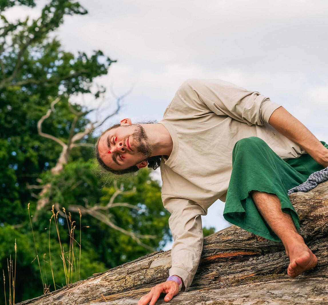 Shaun Hill | Embodied Poetry & Somatic Movement Performance | Queer Spirit Festival 2024 Shaun Hill performing embodied poetry and somatic movement on a fallen tree at Queer Spirit Festival 2024. Ecological movement practice combining dance, poetry, and nature connection in outdoor performance art.